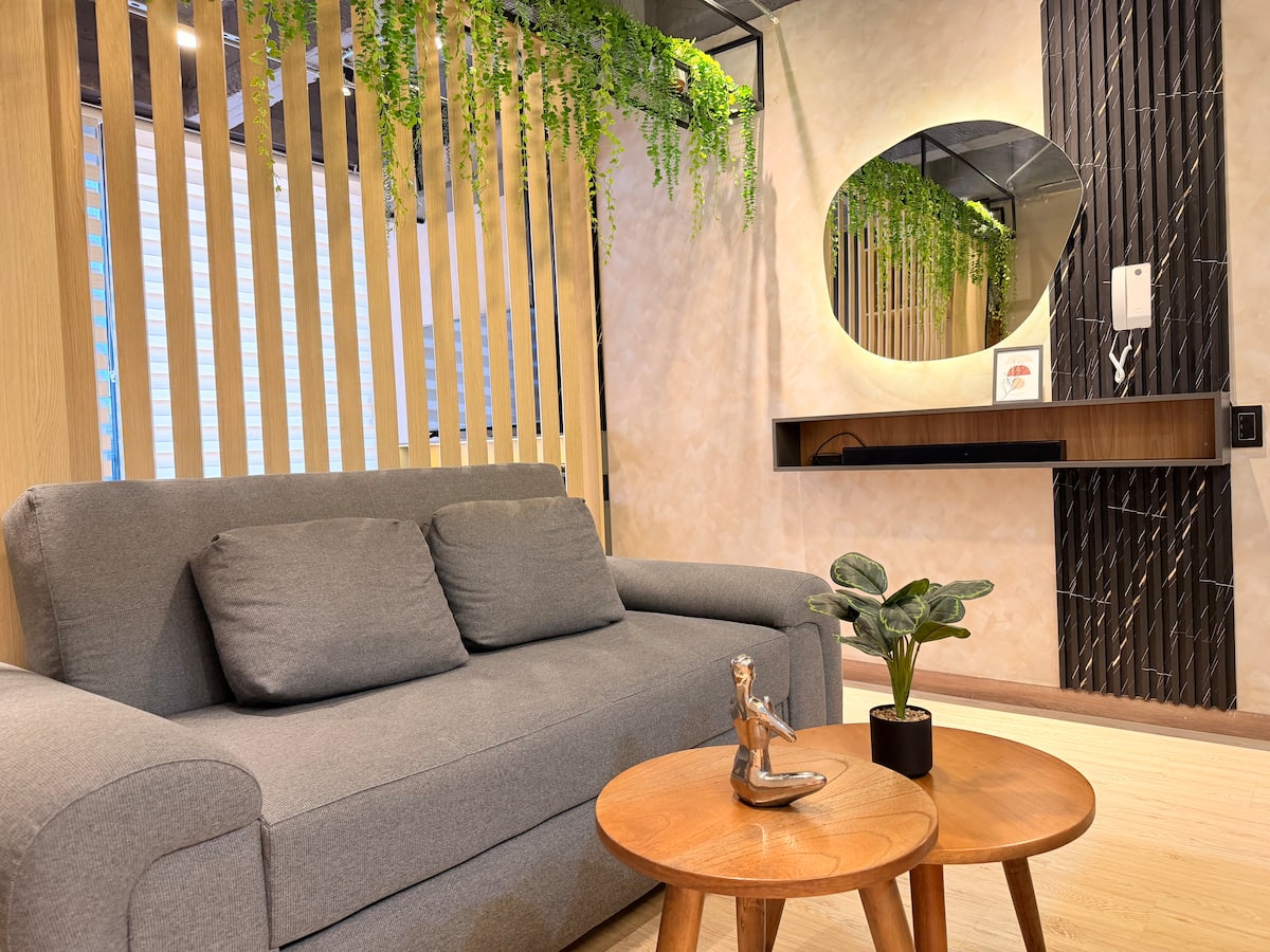 Sala con sofá gris, mesas de centro redondas y espejo iluminado sobre repisa de madera