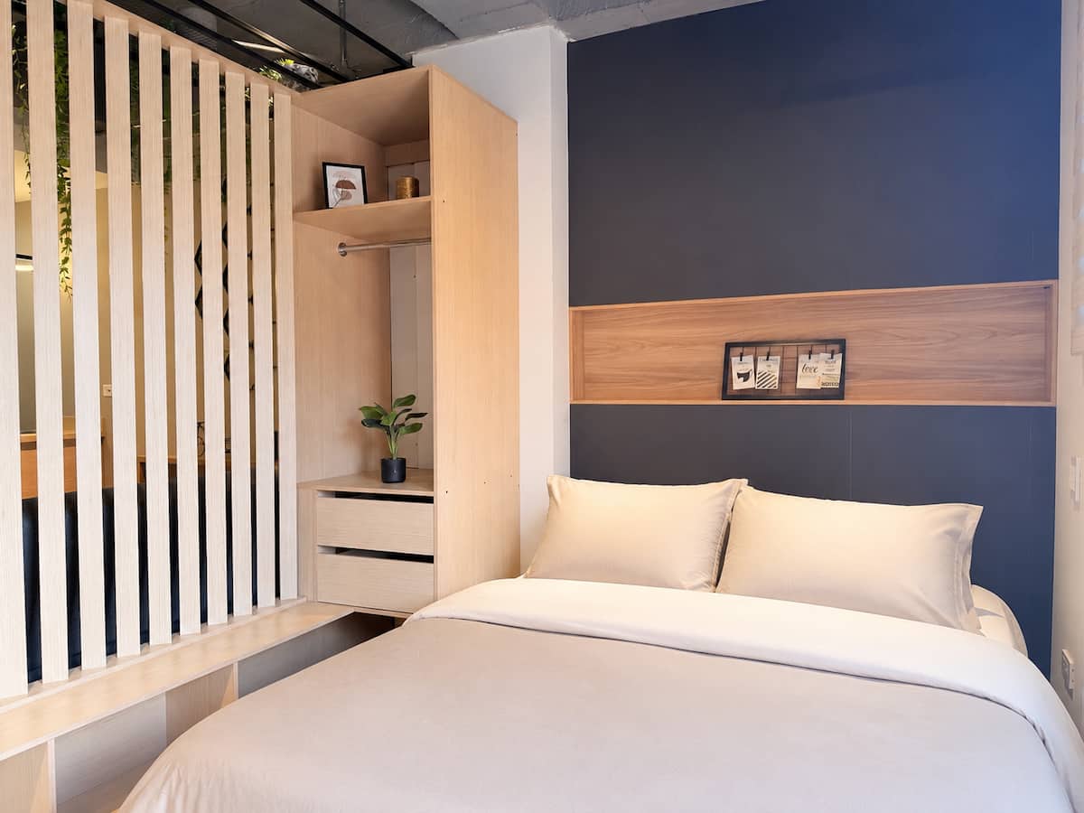Cama doble contra pared azul oscuro, con clóset abierto de madera clara al lado