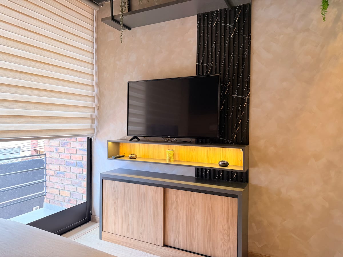 Televisor sobre mueble con luz cálida junto al ventanal que da al balcón en ladrillo