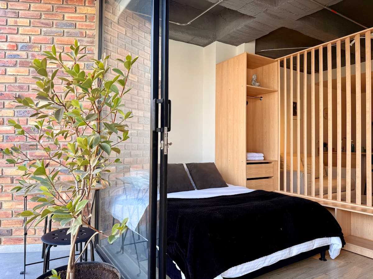 Cama doble con cobija negra vista desde el balcón de ladrillo, con clóset de madera