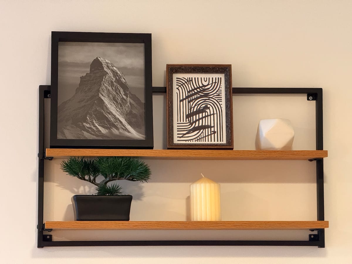 Repisa de madera y metal con cuadros, un bonsái decorativo y una vela encendida