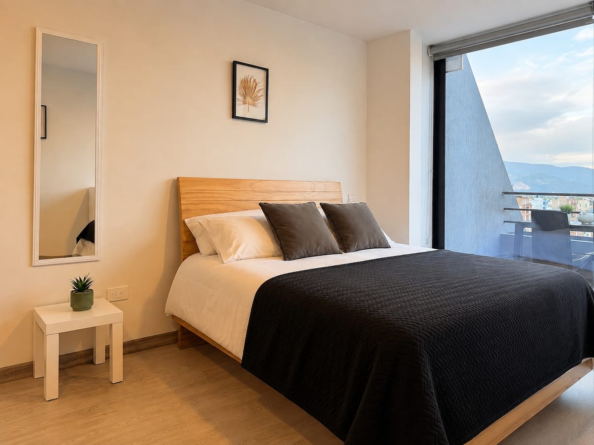 Cama doble con cabecero de madera, espejo de cuerpo entero y salida al balcón