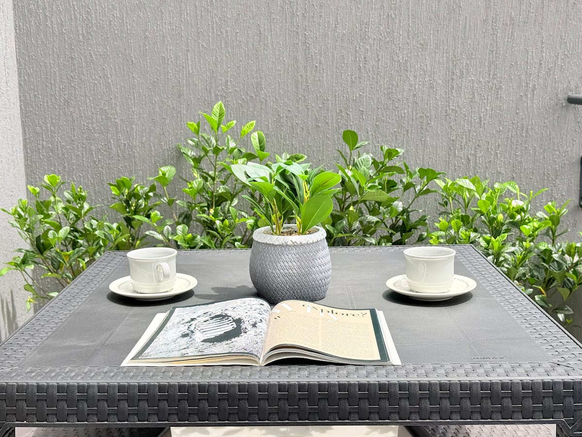 Mesa de terraza con dos pocillos y una revista abierta entre plantas verdes