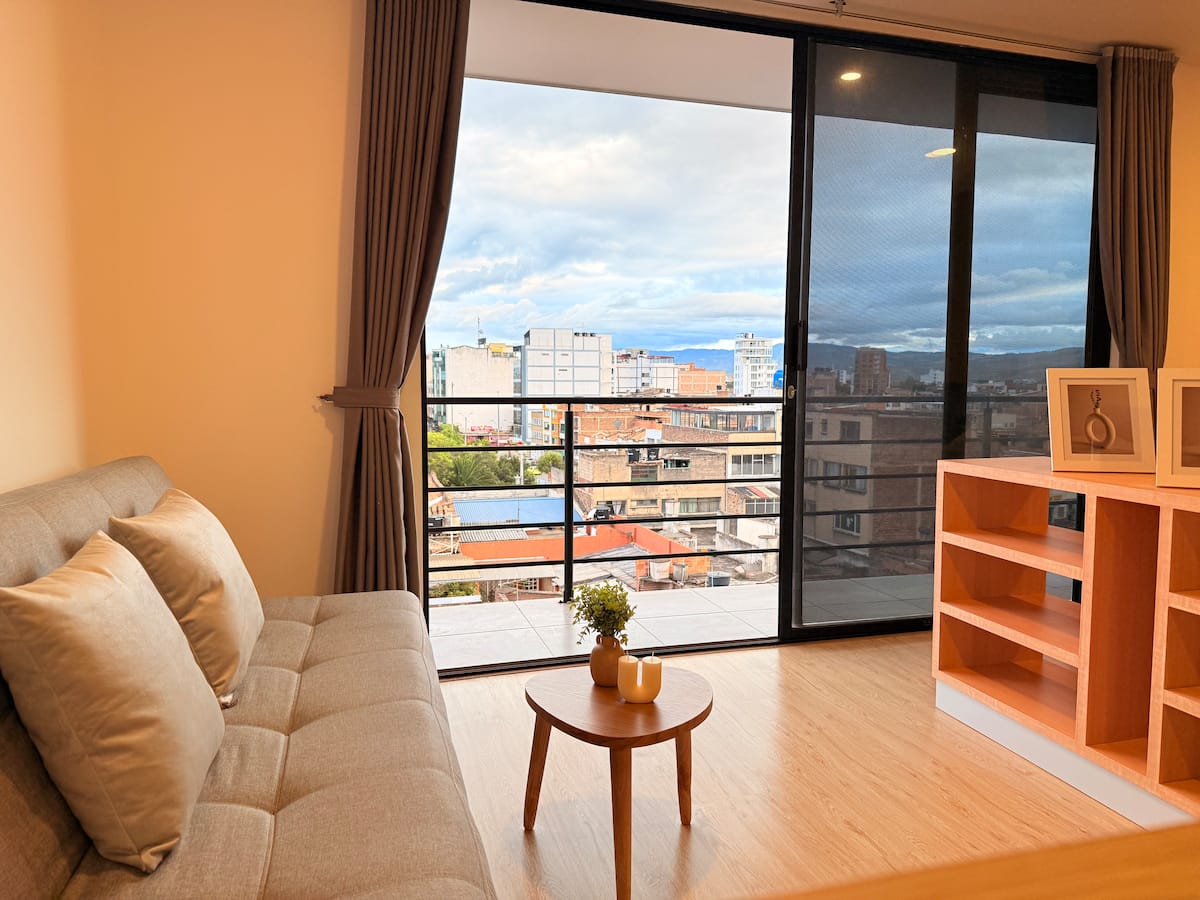 Sala con sofá beige, mesa de centro redonda y ventanal corredizo hacia el balcón