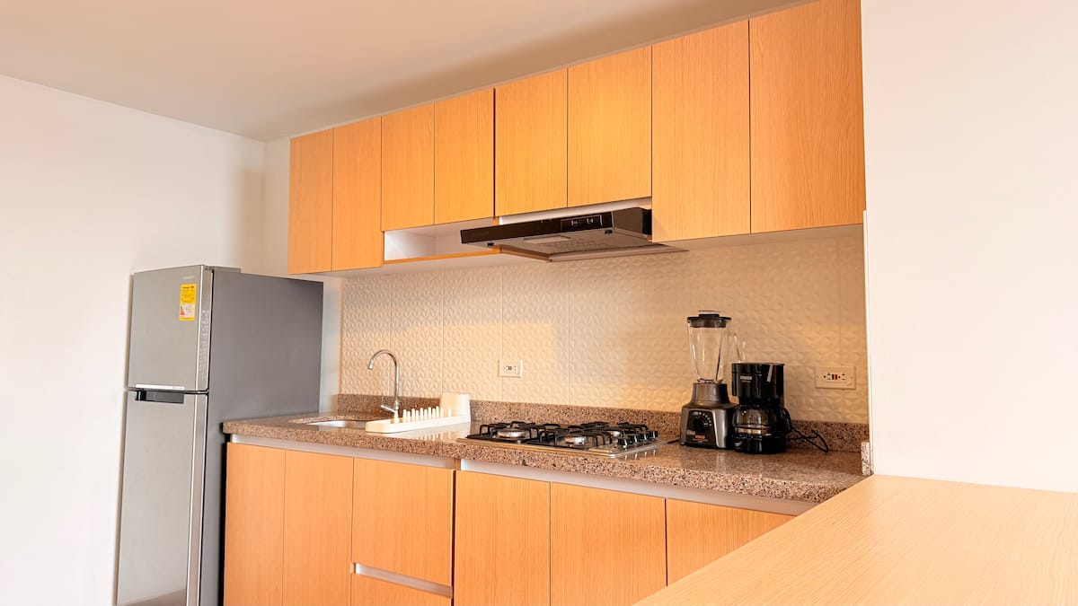 Cocina con gabinetes de madera, mesón de granito, estufa a gas, licuadora y cafetera