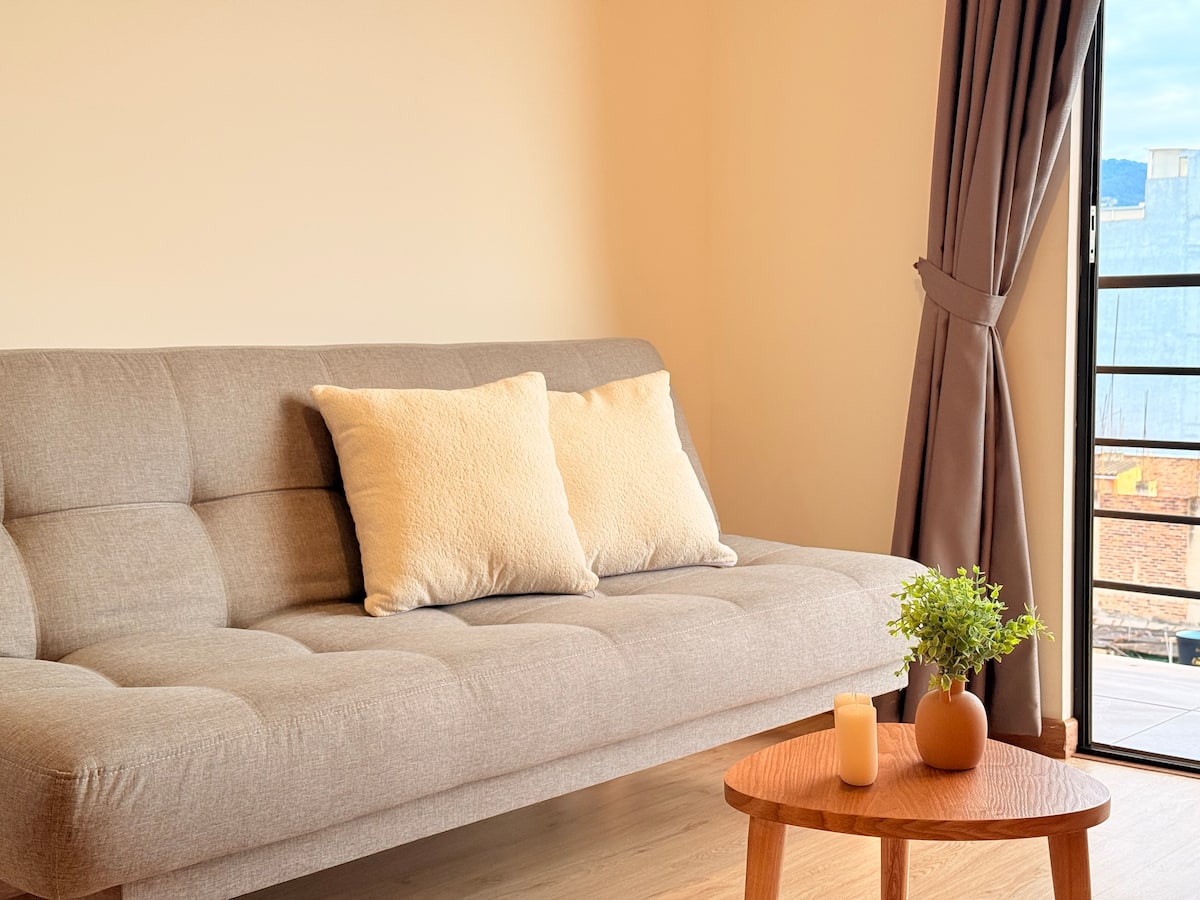 Sofá beige con cojines claros y mesa de centro de madera junto a la cortina del balcón