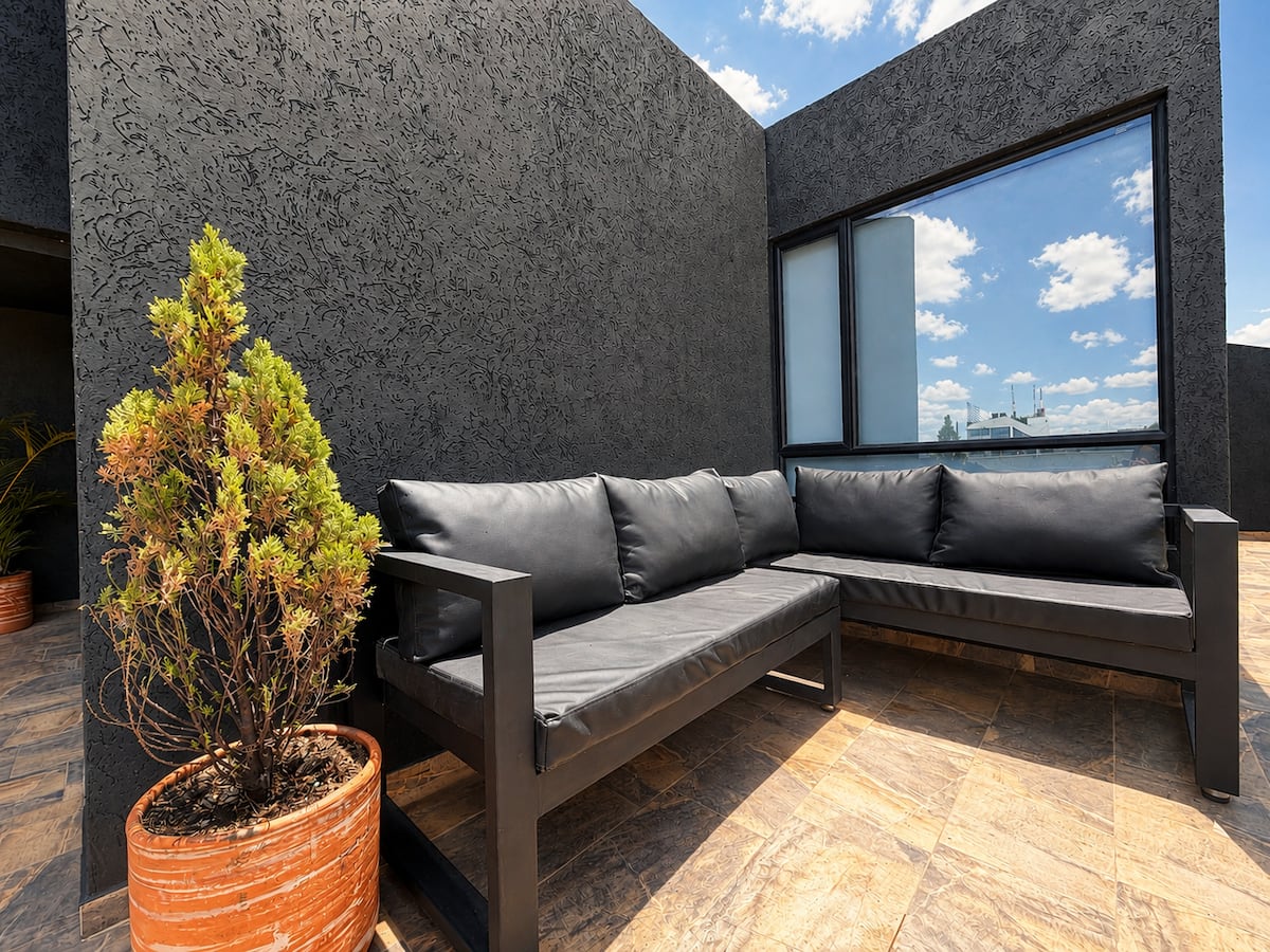 Terraza privada con sofá esquinero gris, matera de barro y cielo despejado