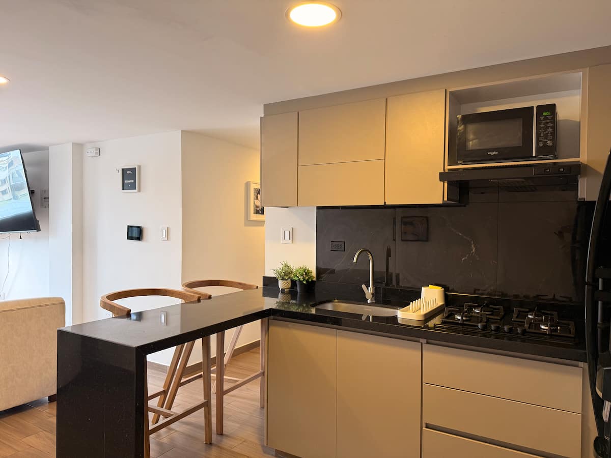 Cocina abierta con barra en granito negro, taburetes de madera y microondas
