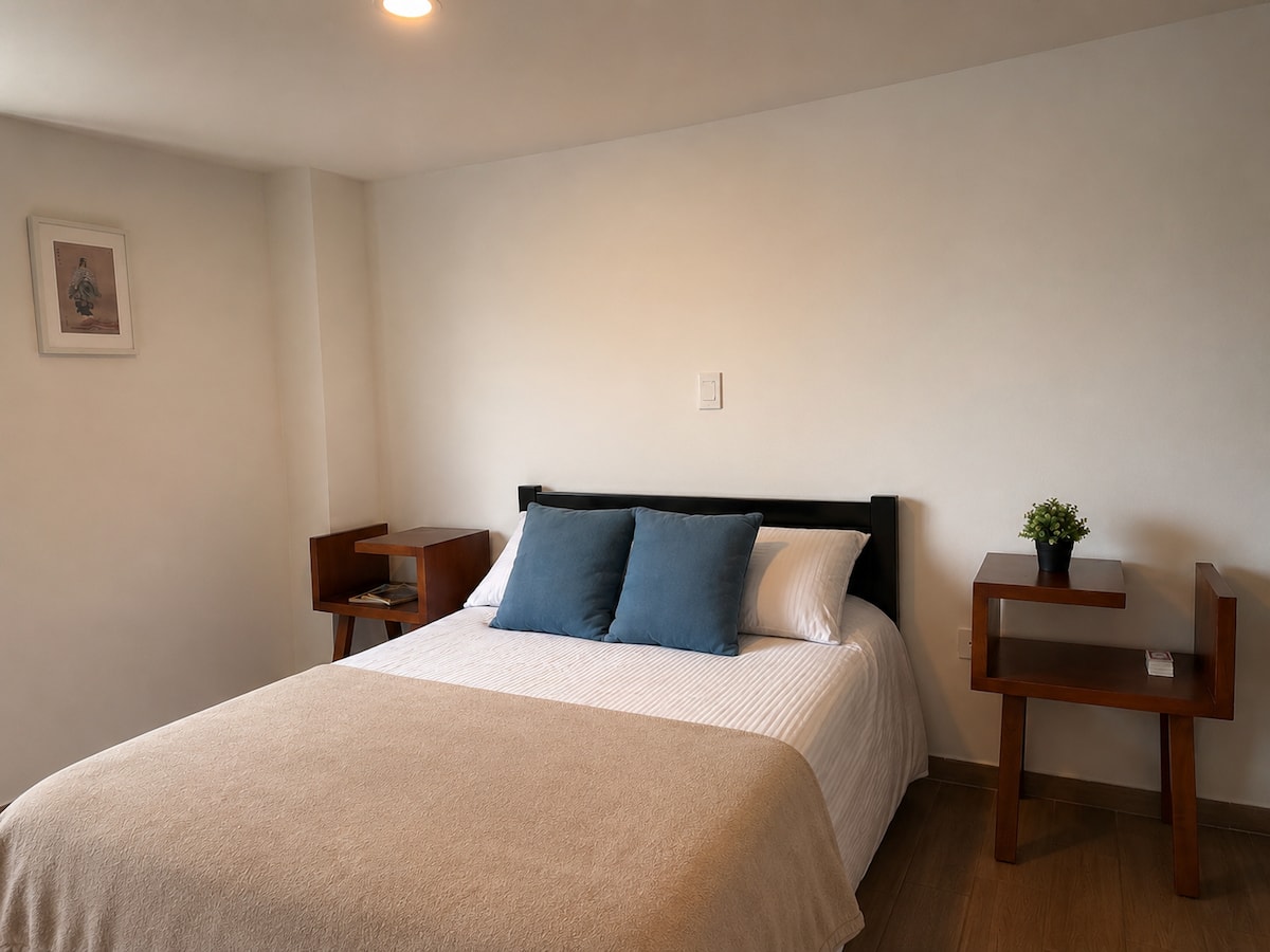 Dormitorio con cama doble, cabecero negro y dos mesas de noche de madera